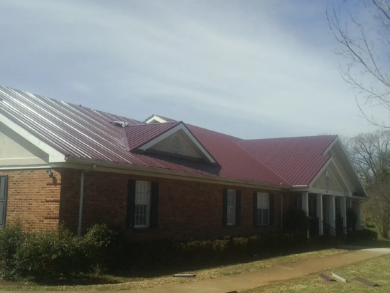 Red metal roof with gabled entries on a long brick building, from a Hail Damage Roof Repair job in Eure