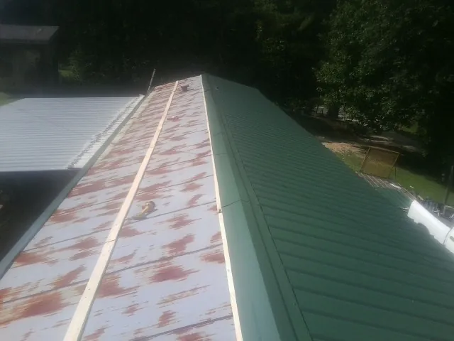 Old rusted panels beside newly installed green metal roofing — Wind Damage Roof Repair by Roofing Brothers in Eure