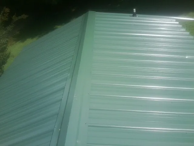 New green metal panels meeting at the ridge of a roof — Flat Roof Repair work by our crew in Eure